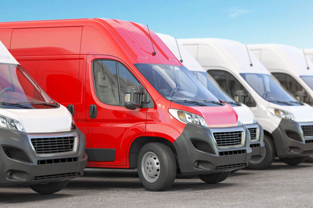 A row of white fleet vans and 1 Red Van